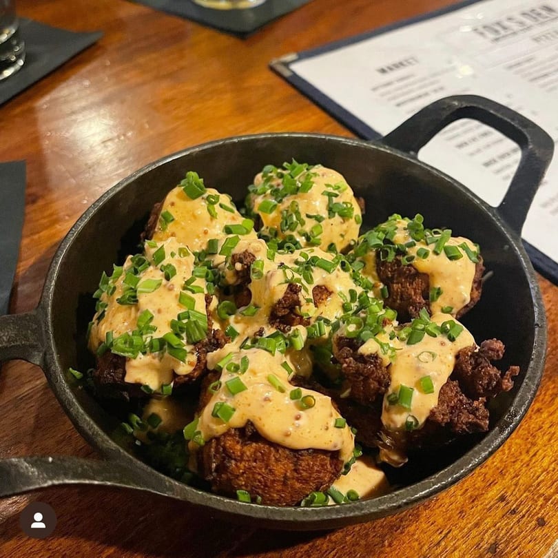 Fox's Den gastropub dish of fried food with creamy sauce and chives in a cast iron pan.