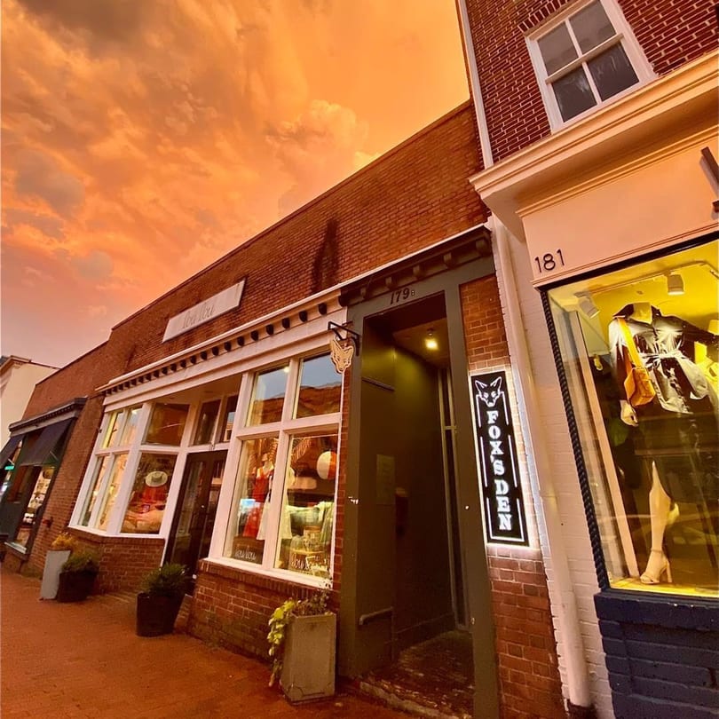 Fox's Den gastropub exterior at dusk, with a glowing sign and orange sky.