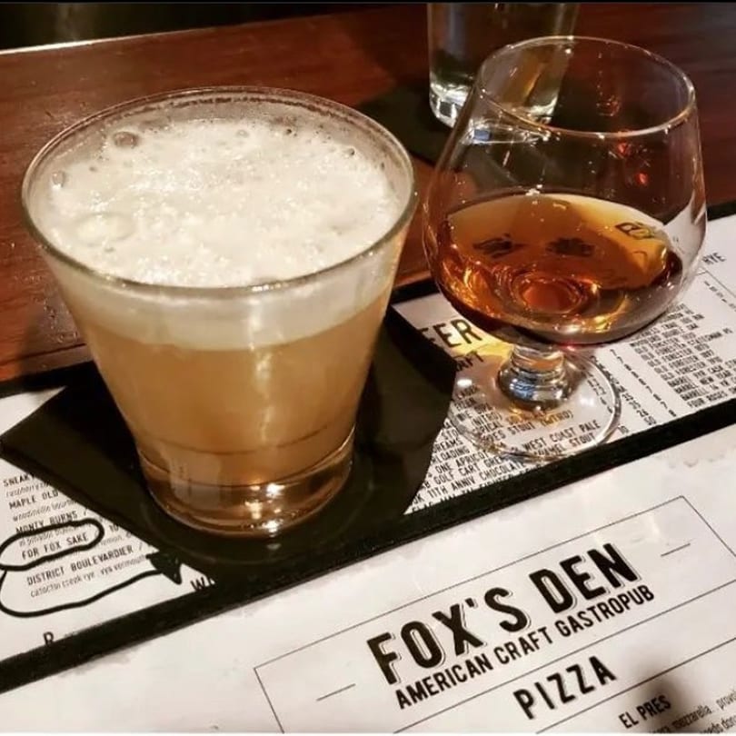 Two drinks, one foamy cocktail and one amber spirit, on a Fox's Den gastropub menu.