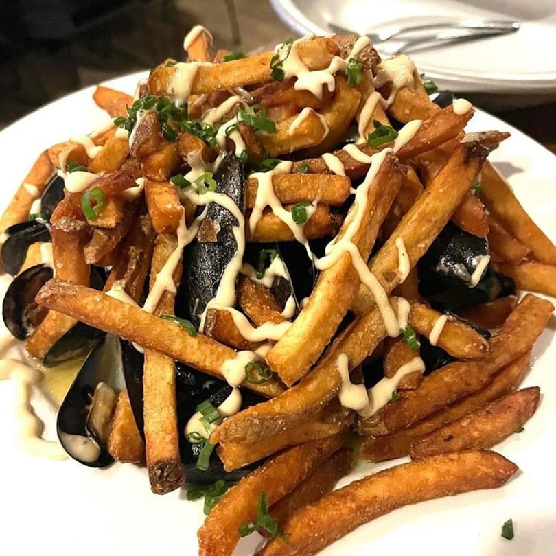 Fox's Den mussels and fries, drizzled with white sauce and garnished with chives.
