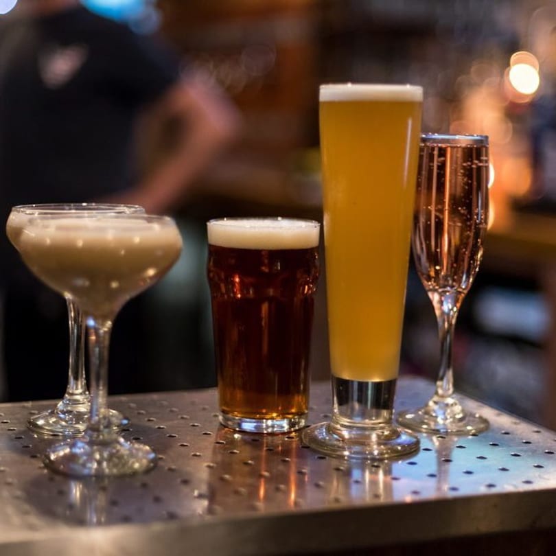 Four different drinks, including cocktails and beers, on a metal bar top at Fox's Den.