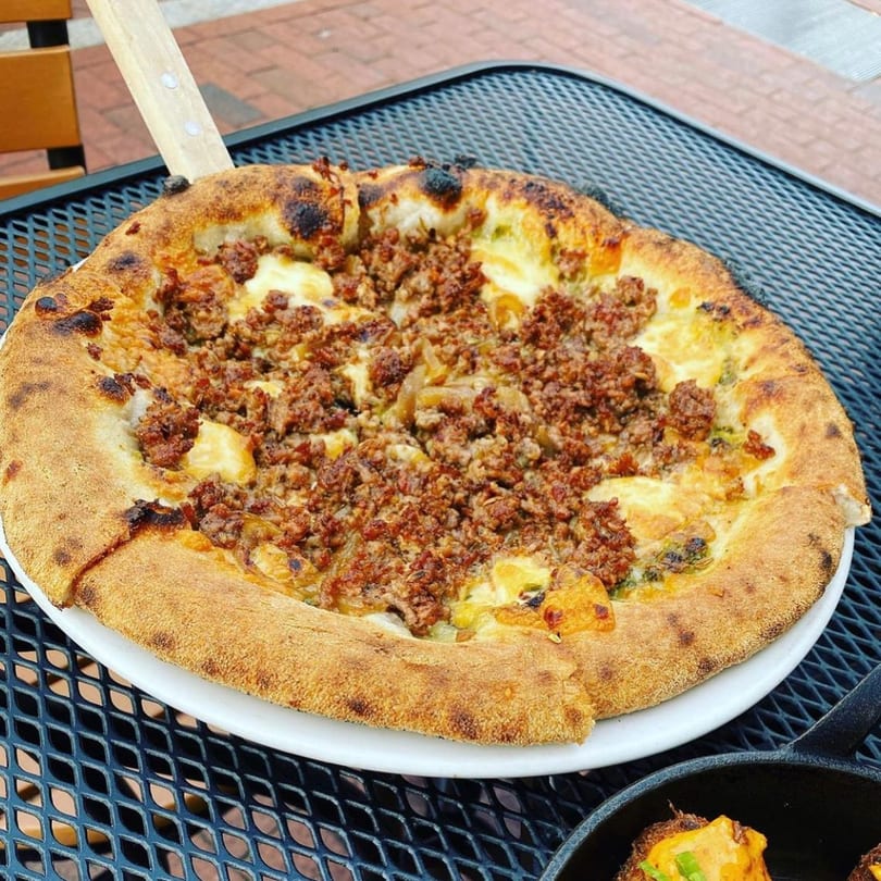 A Fox's Den gastropub pizza with crumbled sausage and cheese on a white plate.