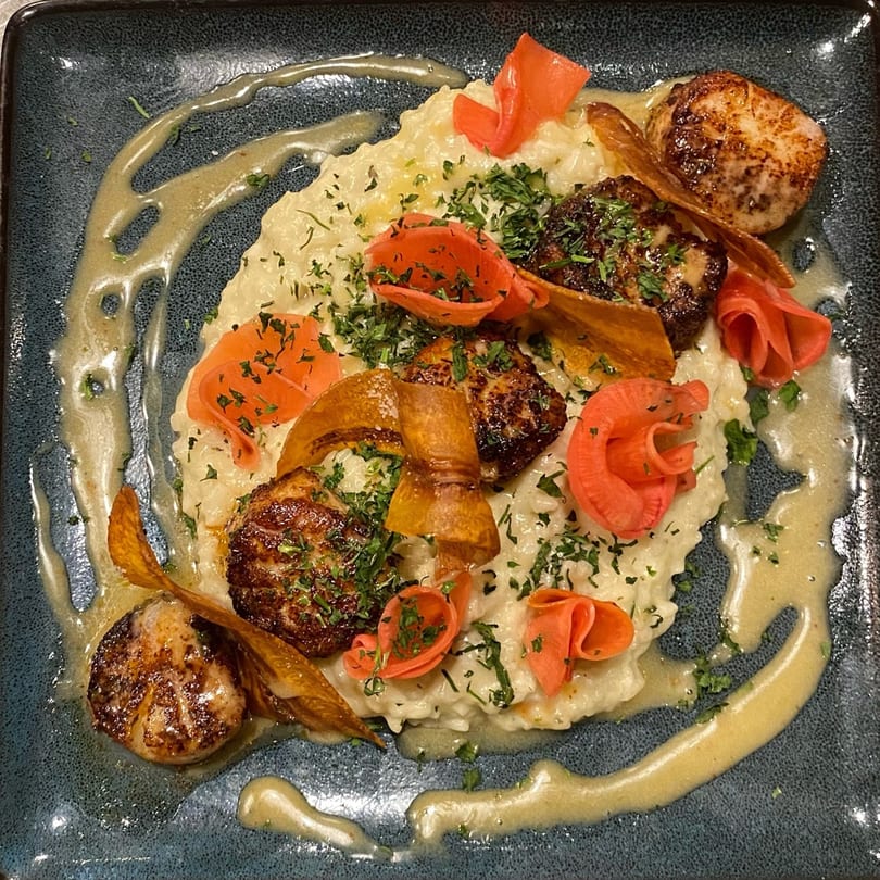 Seared scallops and foie gras on creamy risotto, garnished with pickled radishes and parsnip crisps.